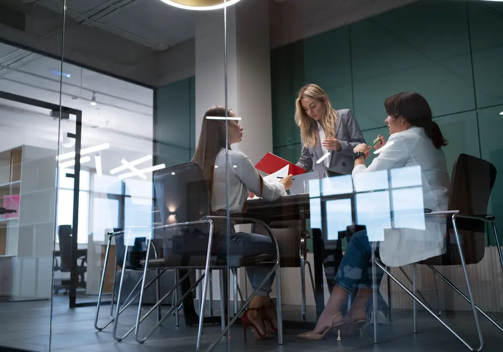 A Go Ahead HiRe headhunter calibrating a European executive search shortlist with two senior client stakeholders in a glass-walled Netherlands boardroom